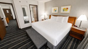 Habitación de hotel con una cama grande, mesitas de noche, un banco, un espejo y dos cuadros en la pared.
