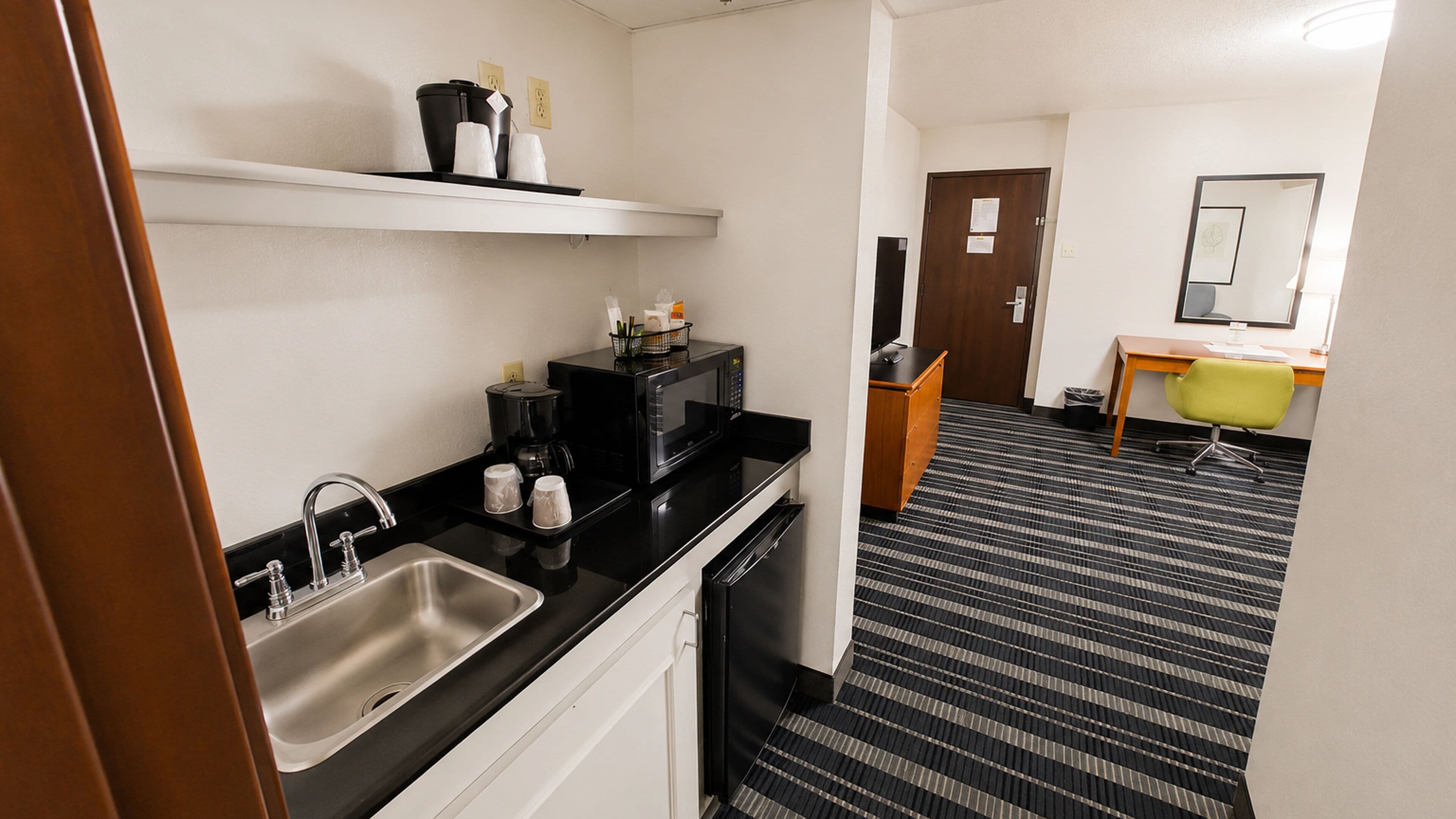 A hotel room with a kitchenette, a sink, a microwave, a coffee maker, and a small table with a chair.