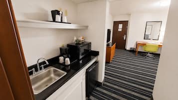 A hotel room with a kitchenette, a sink, a microwave, a coffee maker, and a small table with a chair.