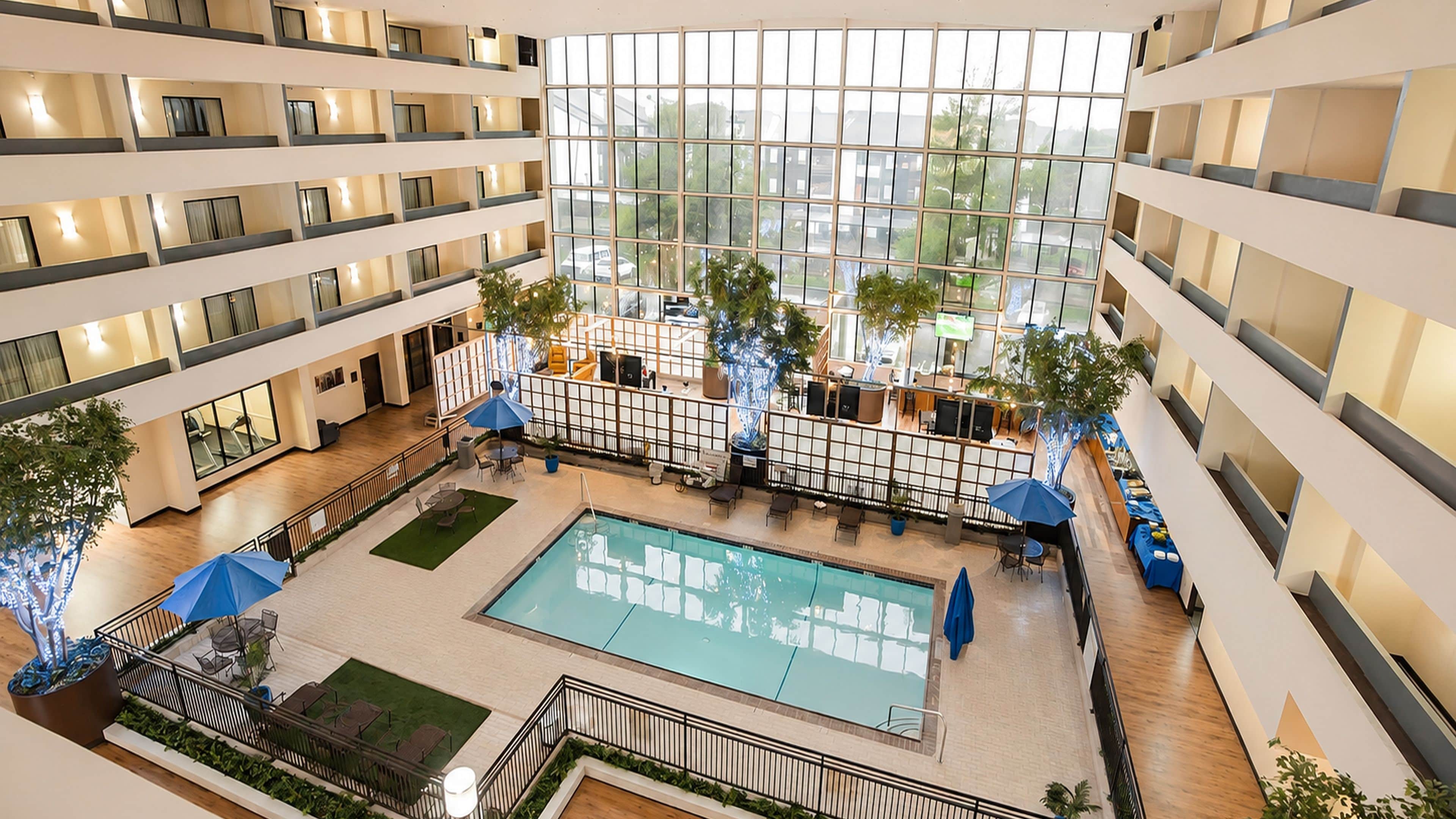 Un atrium d’hôtel à plusieurs niveaux, doté d’une piscine centrale, de plantes d’intérieur et d’espaces aménagés pour s’asseoir.