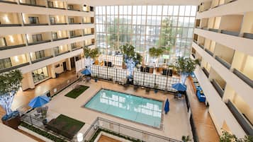 Un atrium d’hôtel à plusieurs niveaux, doté d’une piscine centrale, de plantes d’intérieur et d’espaces aménagés pour s’asseoir.