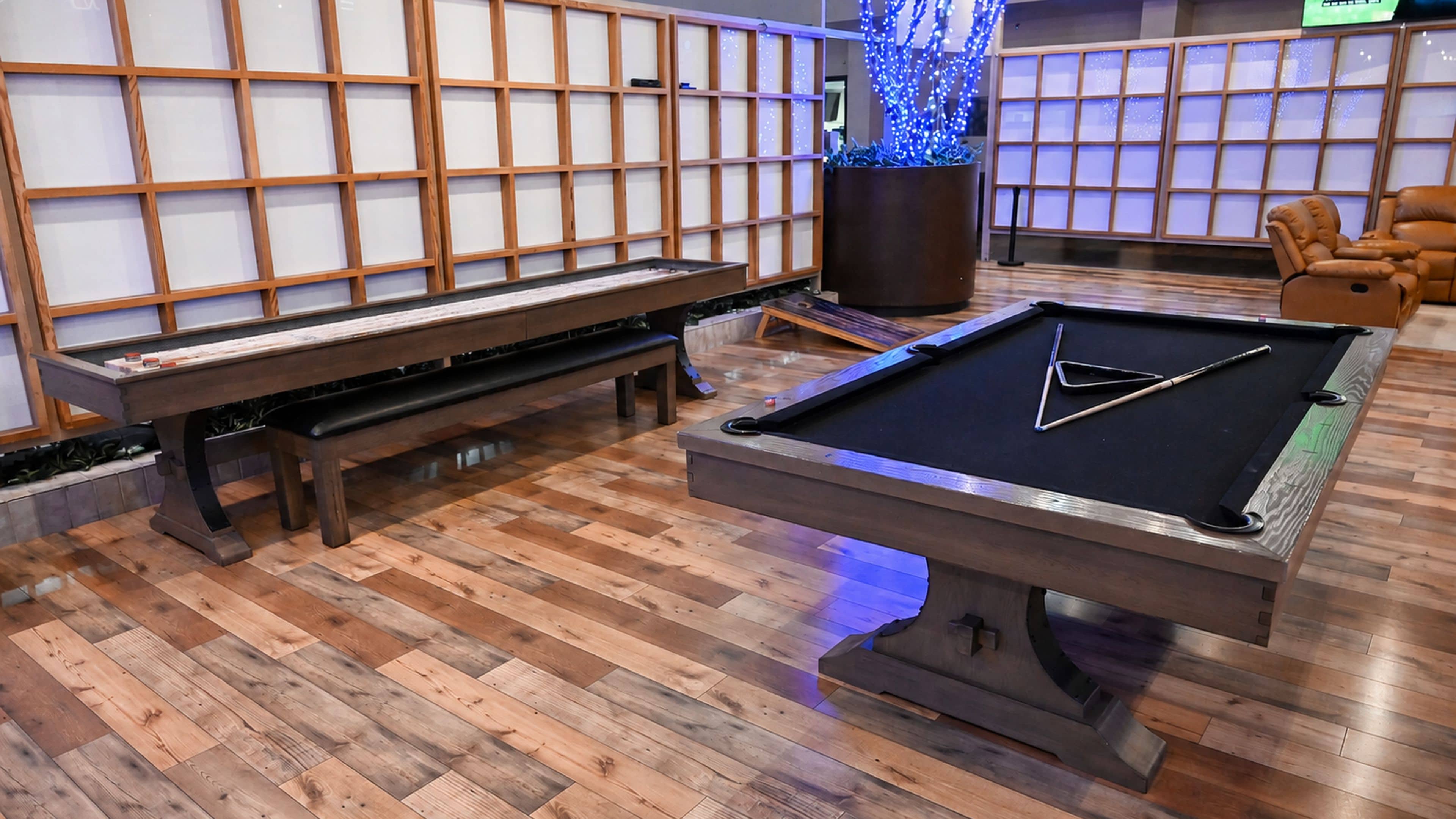 Une table de billard avec un triangle pour placer les billes, une table de jeu de pool et un banc en bois, dans une pièce dotée d’un plancher en bois et d’un mur décoratif.