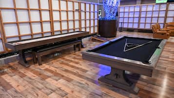 A billiards table with a triangular cue stick, a pool table, and a wooden bench in a room with wooden flooring and a decorative wall.