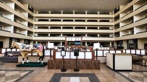 Un vestíbulo de hotel de varios niveles con mostrador de recepción, una estatua de un caballo y una pantalla de televisión.