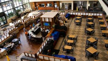 Un vaste espace intérieur aménagé avec différents types de sièges, notamment des tables et des bancs, ainsi qu’un coin bar équipé d’un écran de télévision.
