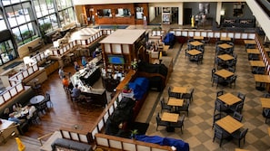 A spacious indoor area with multiple seating arrangements, including tables and benches, and a bar area with a television screen.