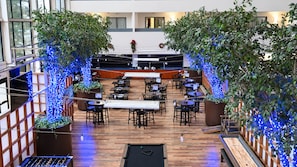 An indoor dining area with tables and chairs, a pool table, and decorative plants. - Atrium Hotel and Suites DFW Airport South (Irving)