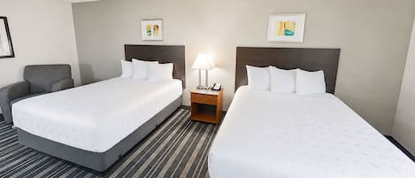 A hotel room with two beds, a nightstand with a lamp, and artwork on the walls.