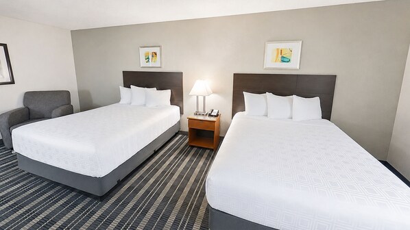 A hotel room with two beds, a nightstand with a lamp, and artwork on the walls.