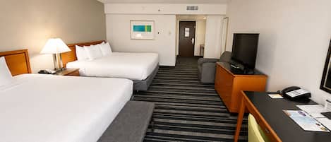 A hotel room with two beds, a desk with a television, a phone, and a carpeted floor.