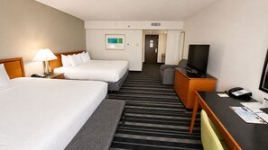 Habitación de hotel con dos camas, un escritorio con televisor, teléfono y piso alfombrado.