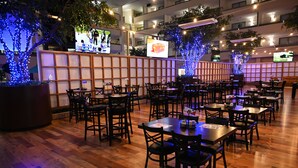 Ein Restaurant mit Holzboden, Tischen, Stühlen und blau beleuchteten Bäumen.