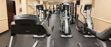 A gym with multiple cardio machines, including treadmills and stationary bikes, arranged in a row.