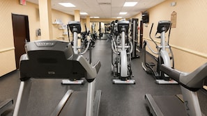 Un gimnasio con varias máquinas de cardio, incluyendo cintas de correr y bicicletas estáticas, dispuestas en fila.