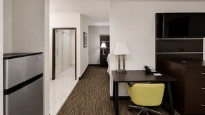 Une chambre d’hôtel équipée d’un réfrigérateur, d’un bureau avec une lampe, d’une chaise, d’un téléviseur et d’un lit en arrière-plan.