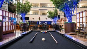 Una mesa de billar en el vestíbulo de un hotel, con zona de bar y asientos.