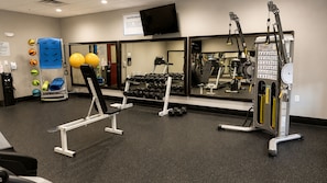 Un gimnasio con equipamiento de ejercicio, televisión y espejo.
