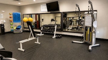 Academia com equipamentos de ginástica, televisão e espelho.