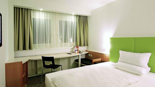 A hotel room with a bed, a desk, a chair, a telephone, and a window with curtains. - ibis Dresden Zentrum (Dresden)