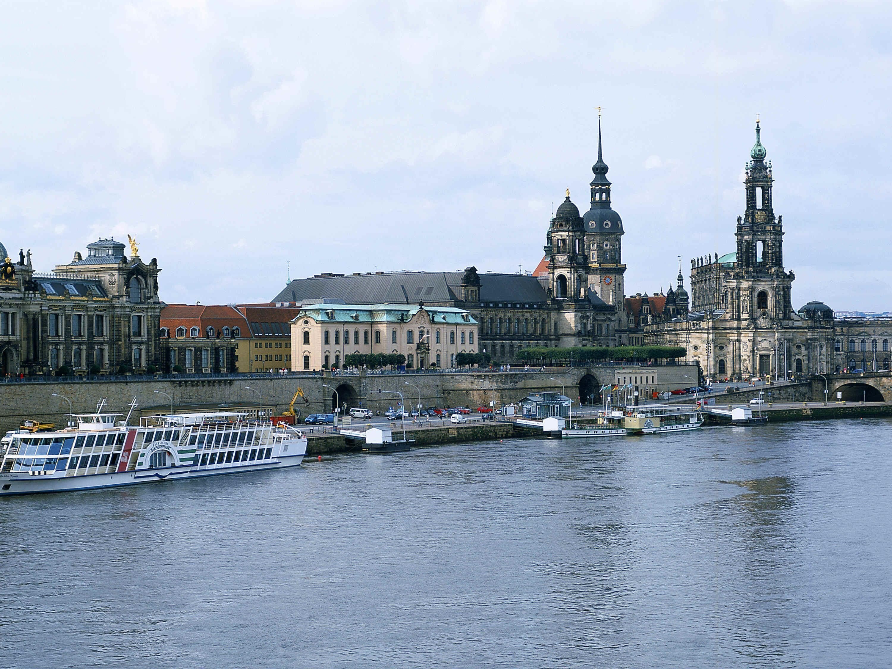 A river with a boat docked, a bridge, and historic buildings with domes and spires.