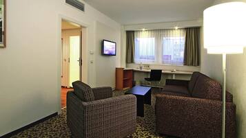 Una habitación de hotel con sofá, sillón, escritorio y televisión.
