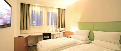 A hotel room with two beds, a desk, a chair, and a window with curtains.