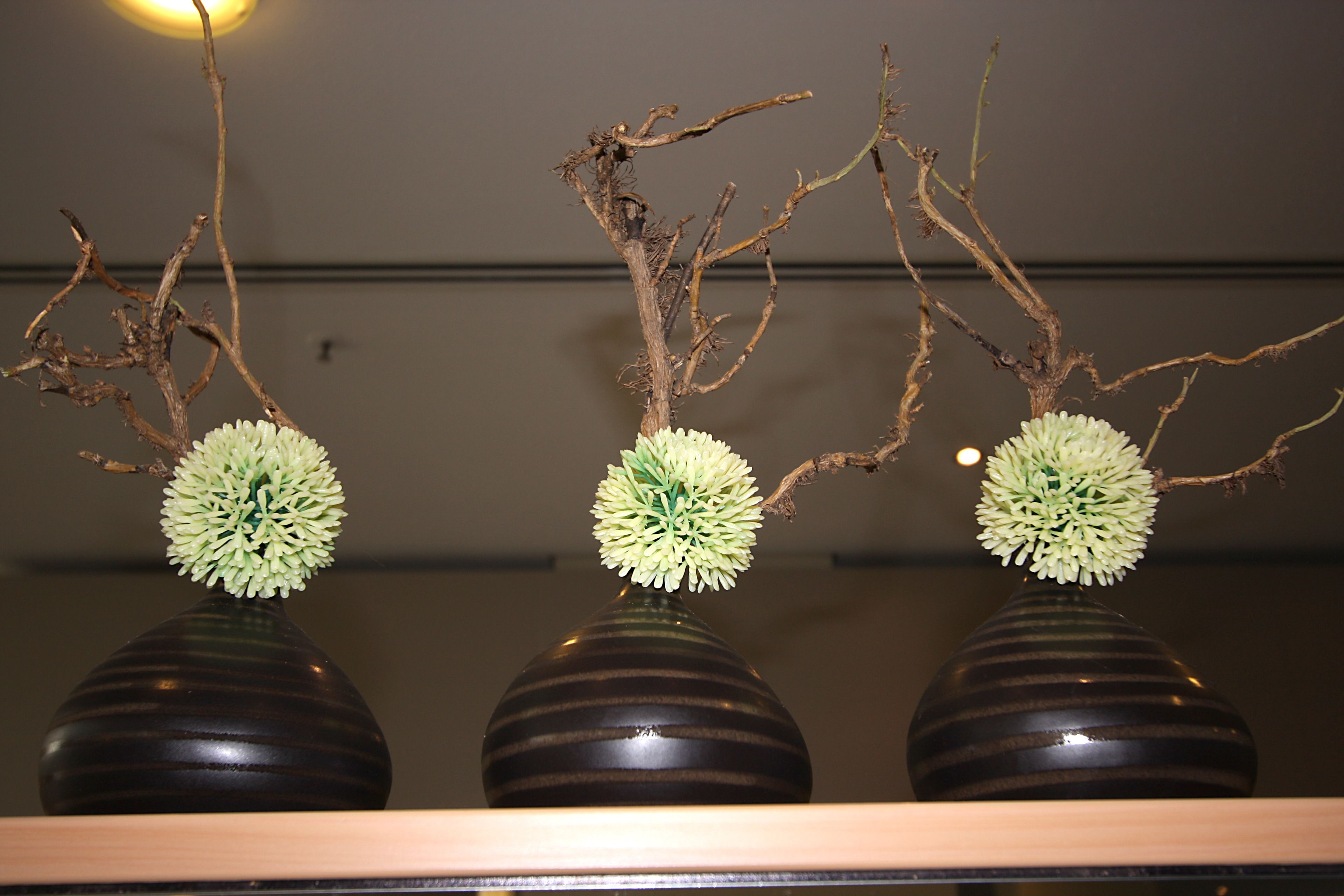 Drei Vasen mit kugelförmigen Blumenarrangements auf einem Regal.
