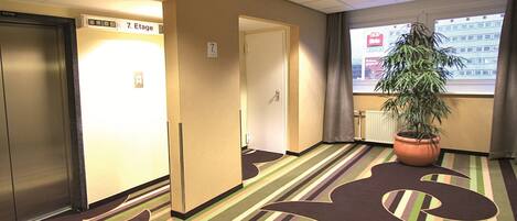 A hotel hallway with striped carpet, a potted plant, and doors labeled "7. Etage".