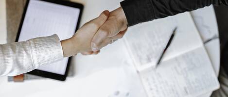 Two hands shaking over a table with documents and a smartphone.