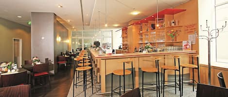 A restaurant with a bar area, multiple seating options including bar stools and tables, and a variety of dishes displayed on shelves.