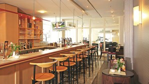 A bar area with multiple stools, a television mounted on the wall, and shelves with glasses and bottles. - ibis Dresden Zentrum (Dresden)