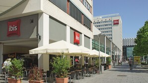 An outdoor seating area with umbrellas and potted plants, a building with 'ibis' signage, and a clear sky. - ibis Dresden Zentrum (Dresden)