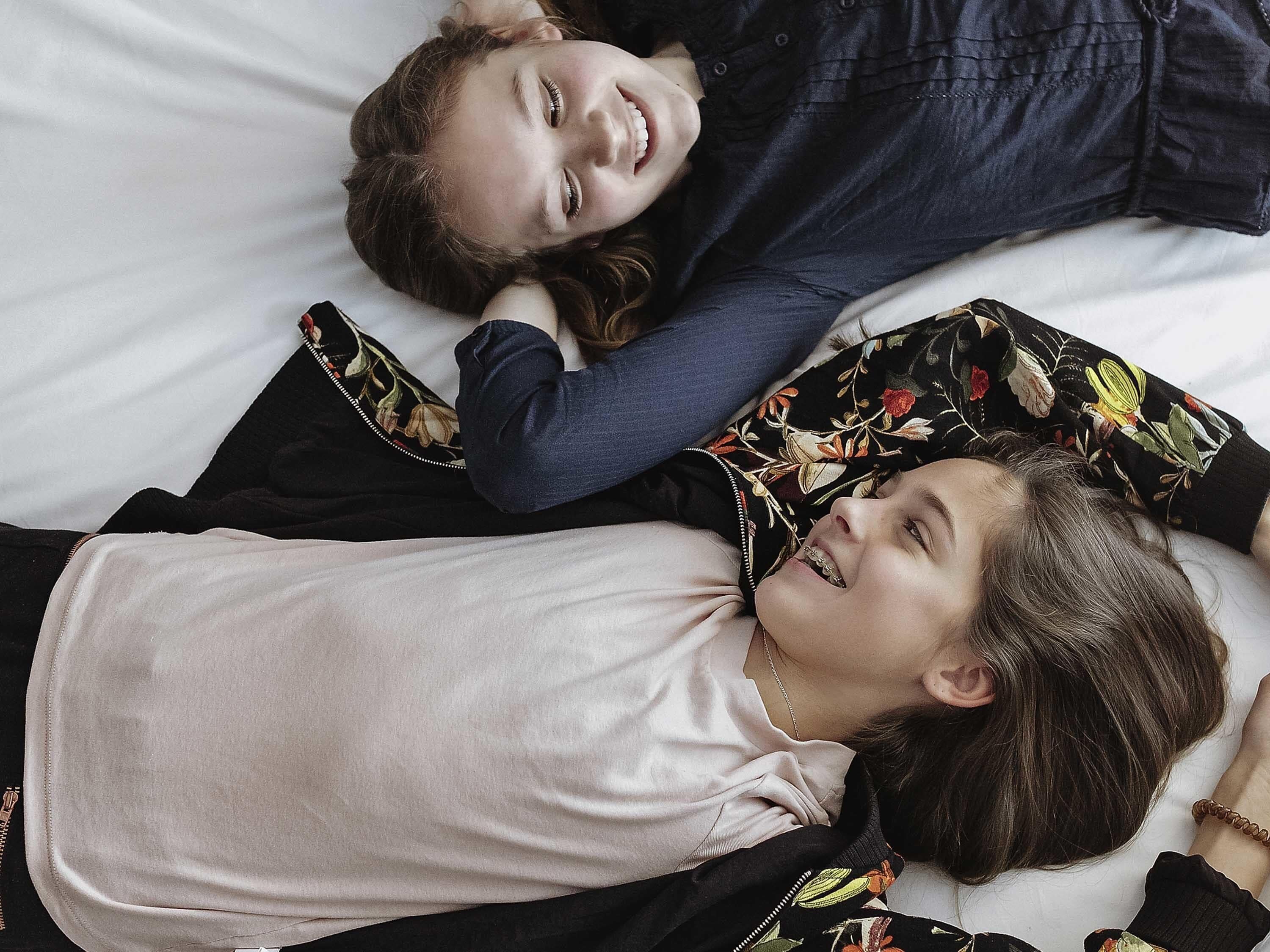 Two individuals lying on a bed with a floral-patterned pillow and a plain white sheet.