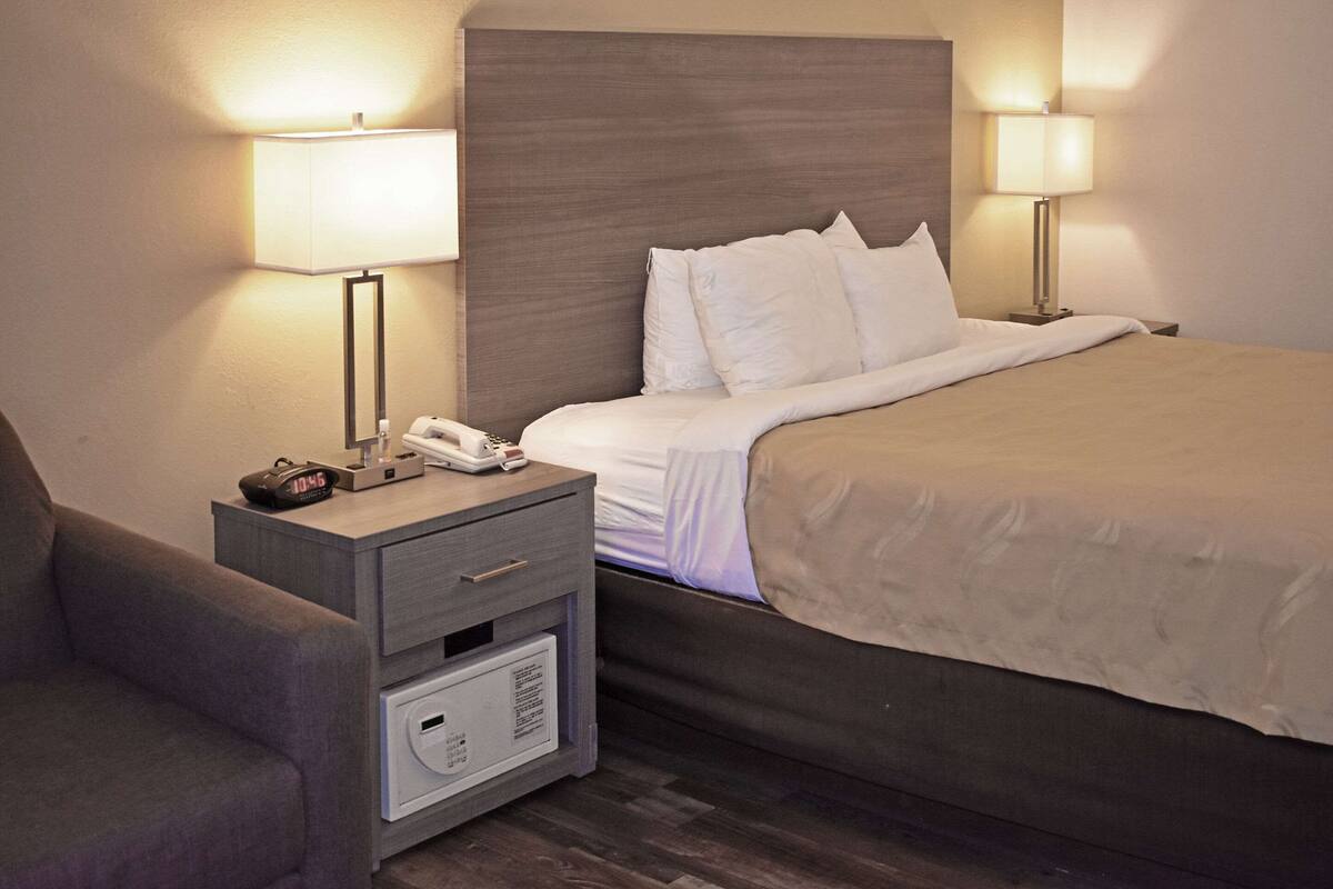 Une chambre d’hôtel comprenant un lit, des lampes de chevet, une table de chevet avec un téléphone et une horloge, et une chaise.