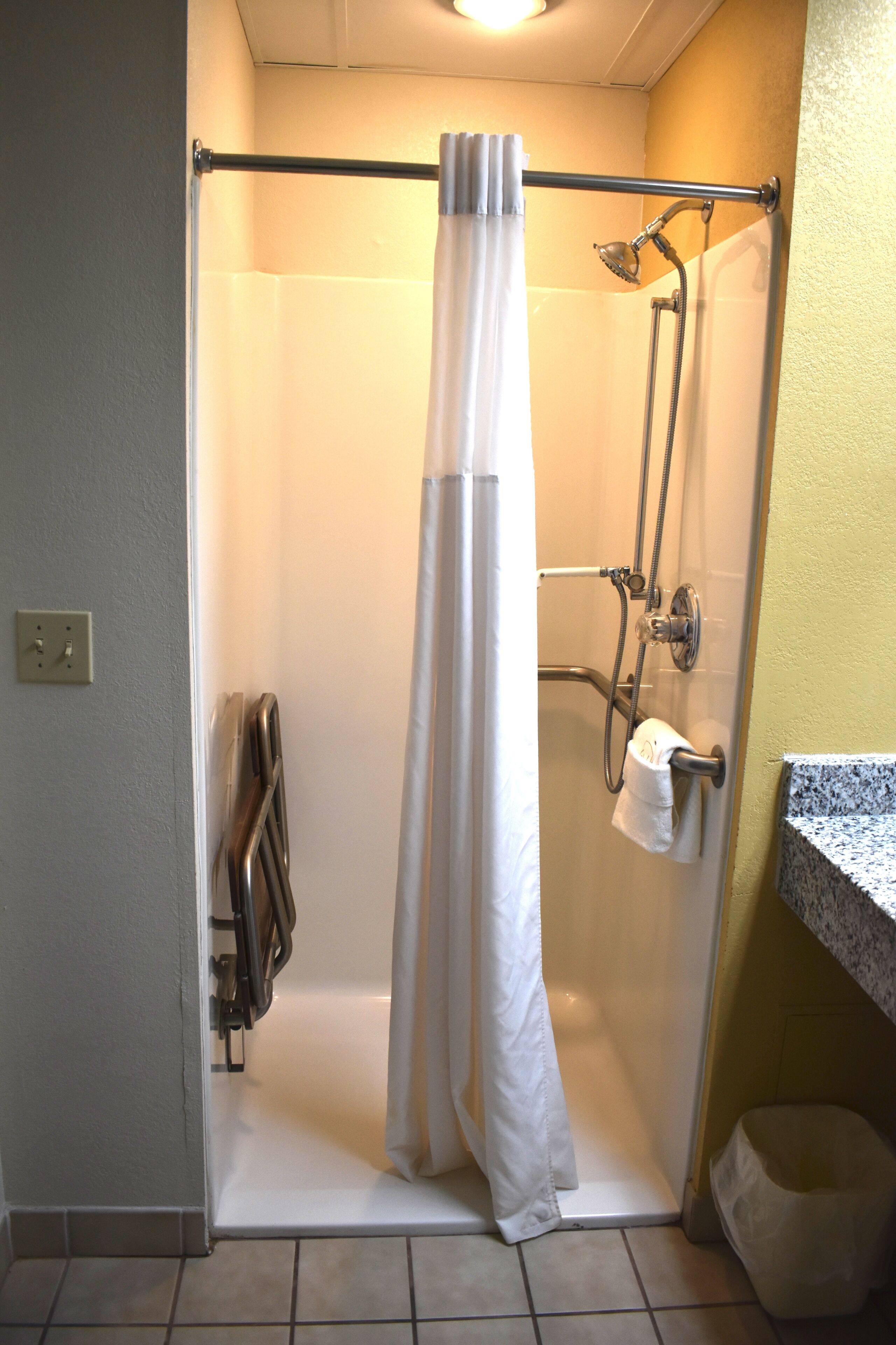 A shower with a curtain, a towel rack, and a handheld showerhead.