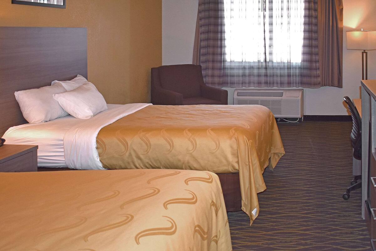 Une chambre d’hôtel avec deux lits, une chaise, un bureau et une lampe.