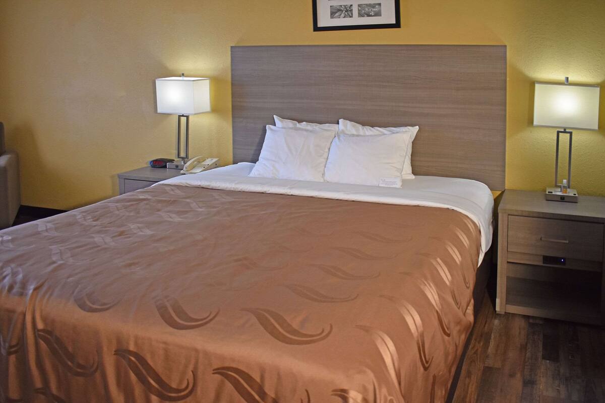 Un lit bien fait, recouvert d’une couvre-lit à motifs, avec deux lampes de chevet et une table de chevet sur laquelle se trouvent un téléphone et un petit appareil.