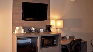 Camera d'albergo con televisione a schermo piatto montata a parete, forno a microonde, macchina del caffè, lampada e scrivania con sedia.