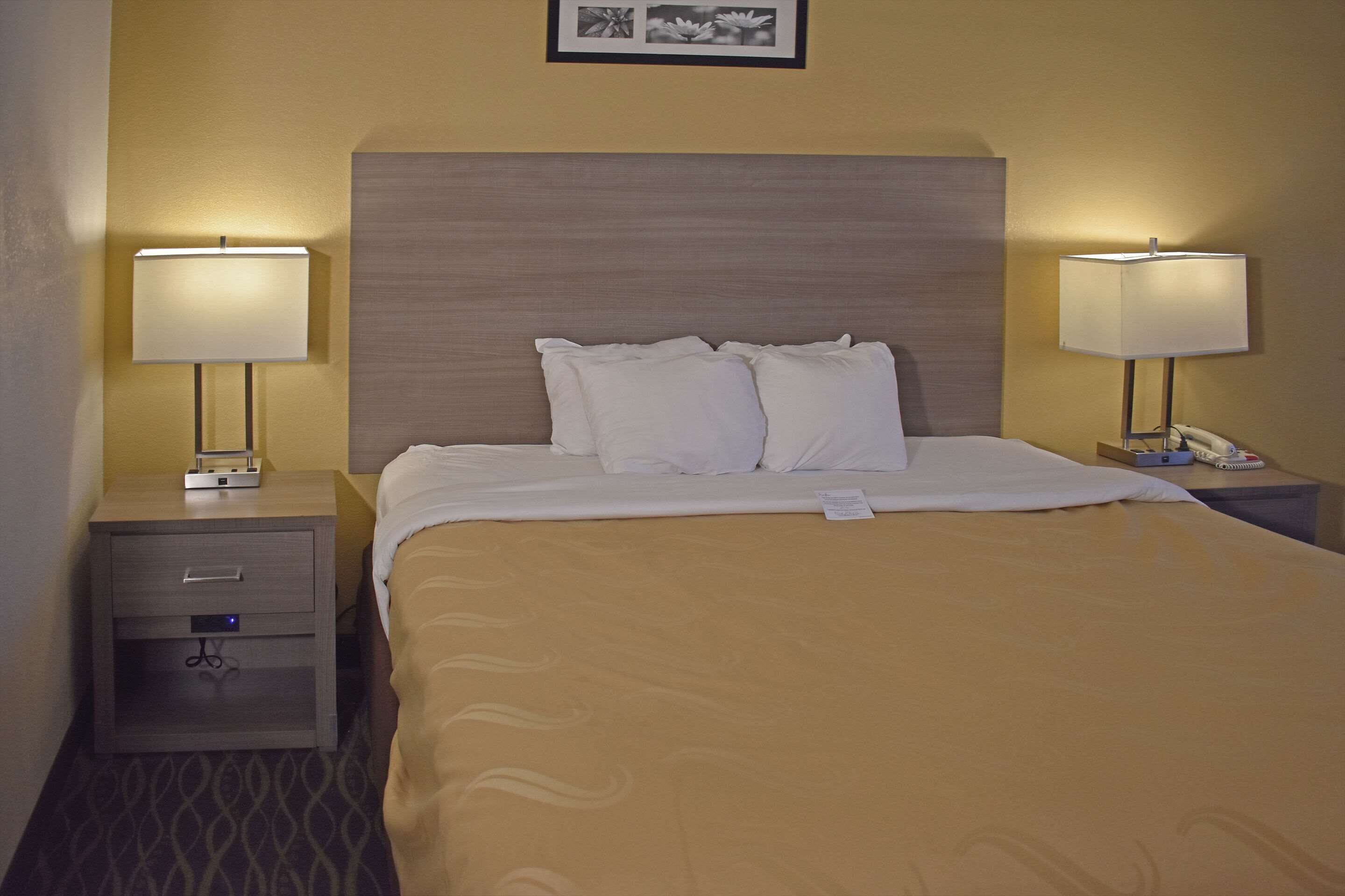 A hotel room with a bed, two bedside tables, a nightstand, and two lamps.
