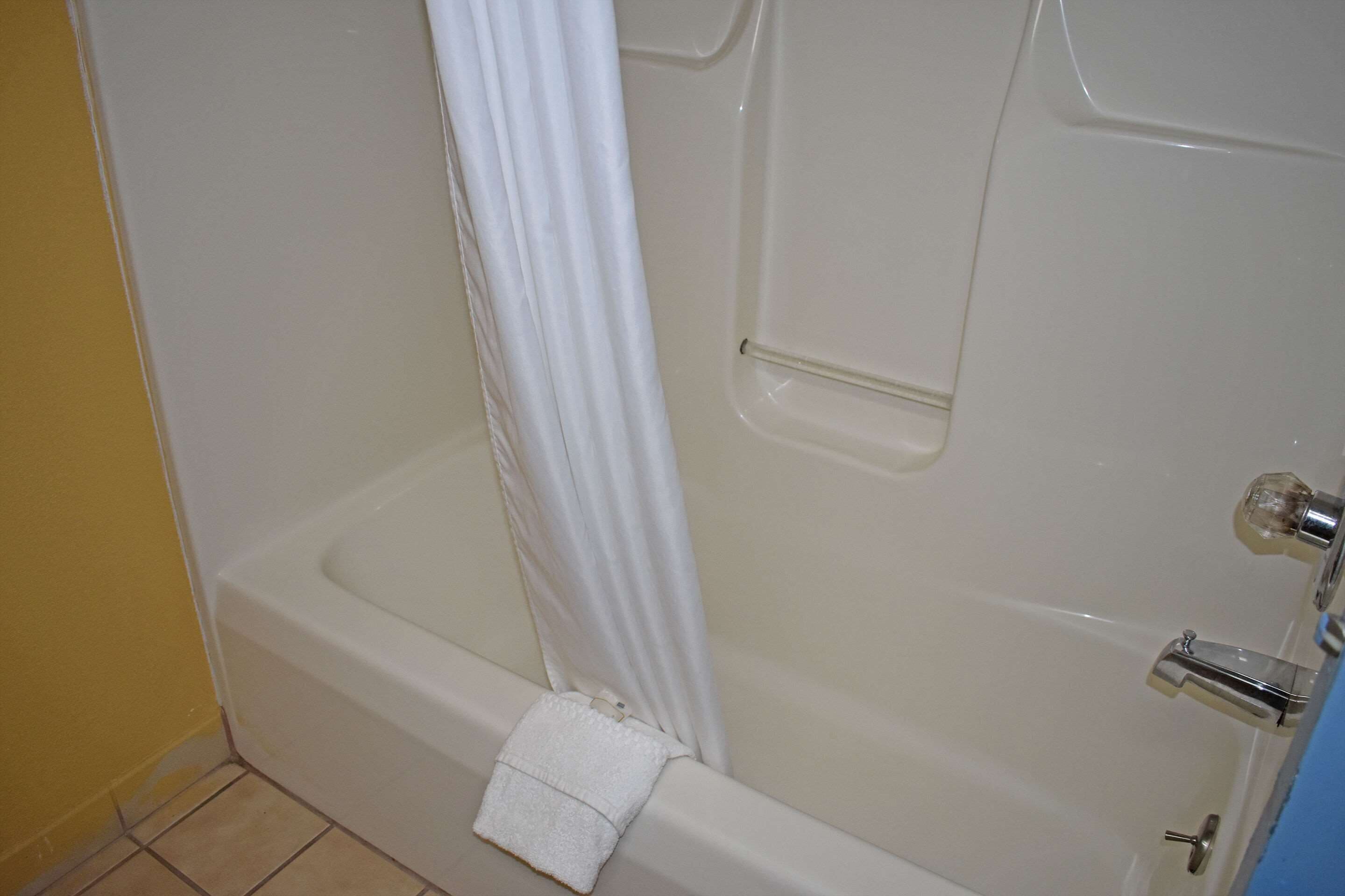 A standard white bathtub with a shower curtain, a handheld showerhead, and a towel placed on the floor.