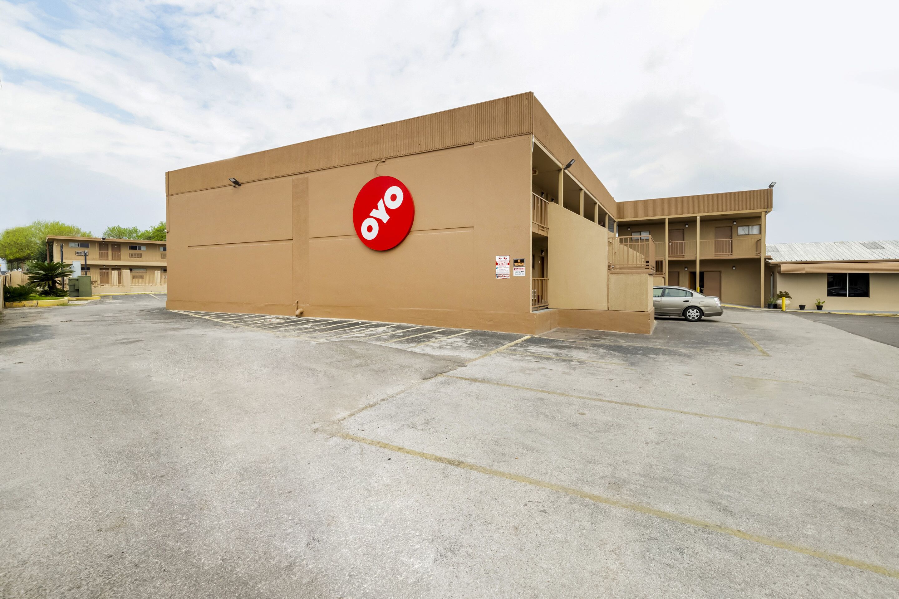 A building with a large red circular logo, a parking lot, and a car in the background.