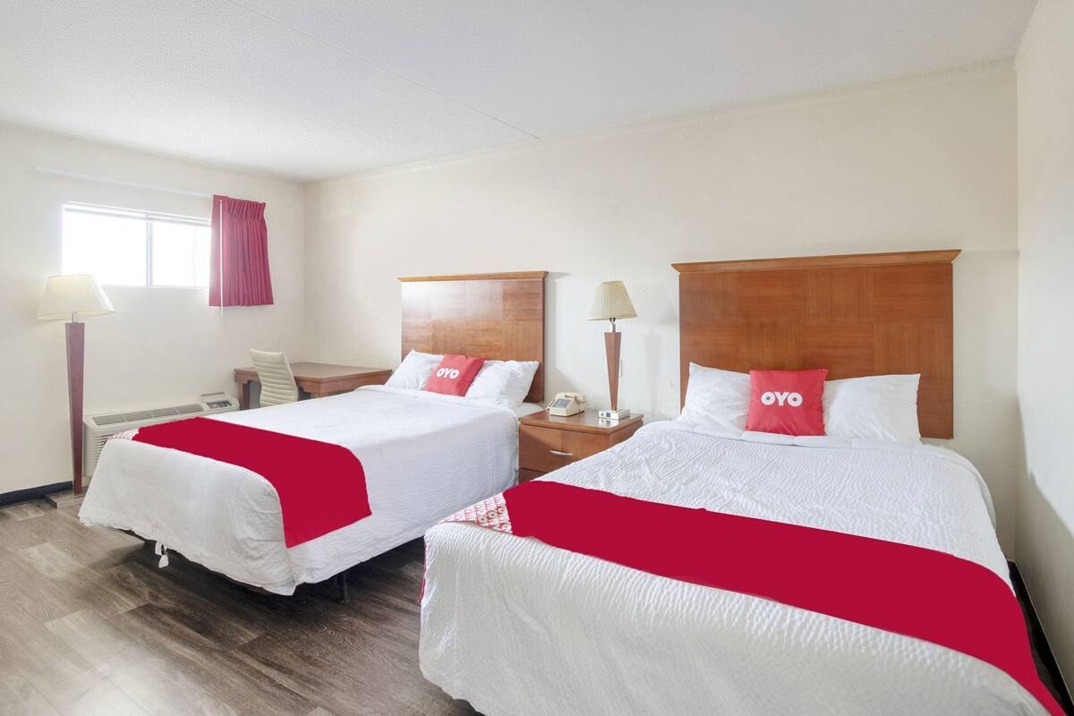 A hotel room with two beds, a desk, a chair, a lamp, and a window with curtains.