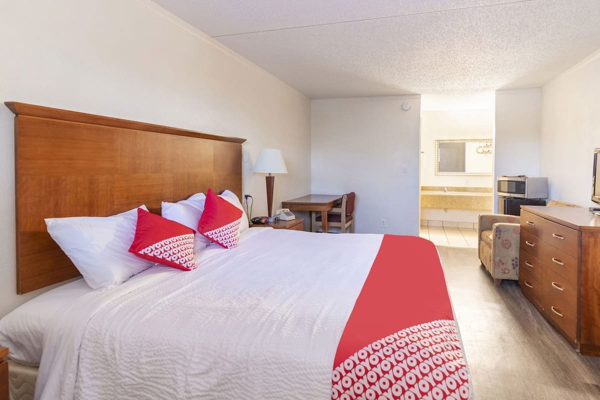 A hotel room with a bed, a desk, a chair, a dresser, a microwave, and a TV.