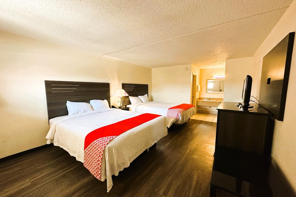 A hotel room with two beds, a TV, and a desk.
