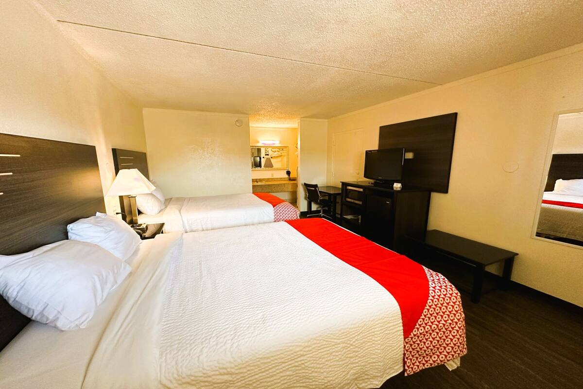 A hotel room with two beds, a TV, a desk, and a bathroom visible through an open door.