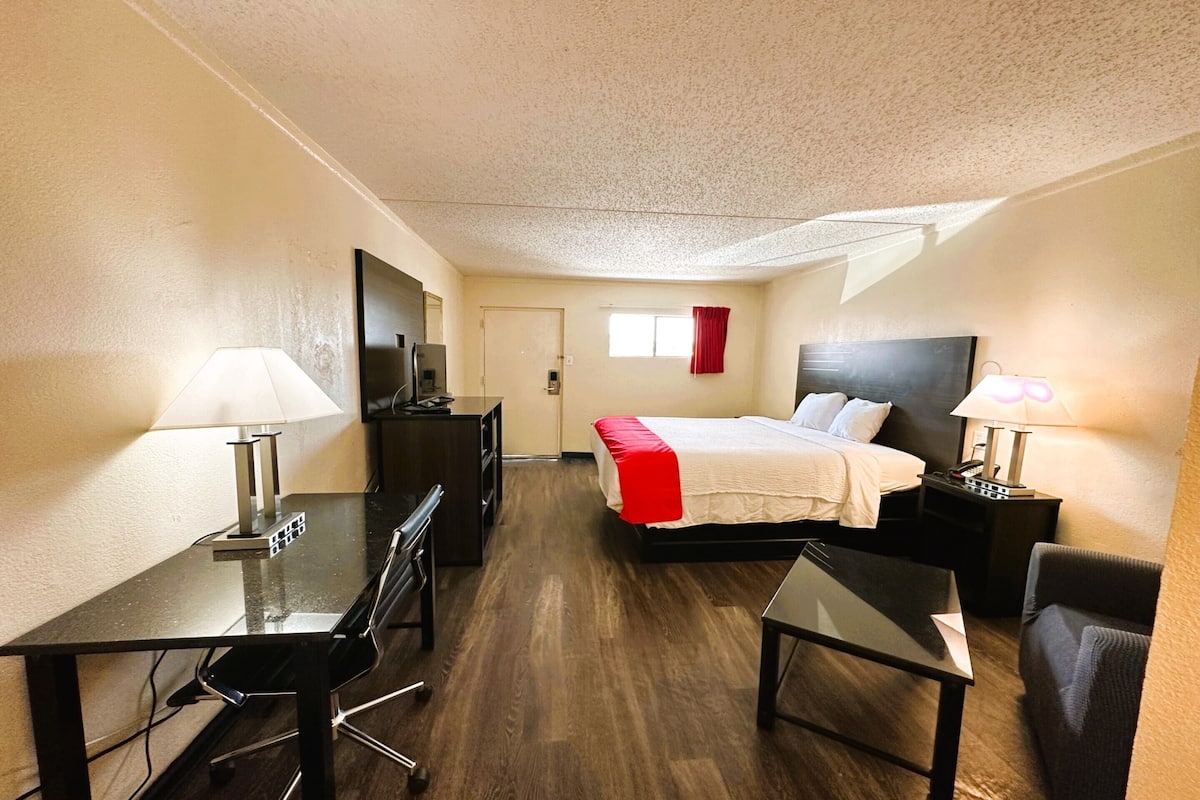 A hotel room with a bed, desk, chair, and a TV.
