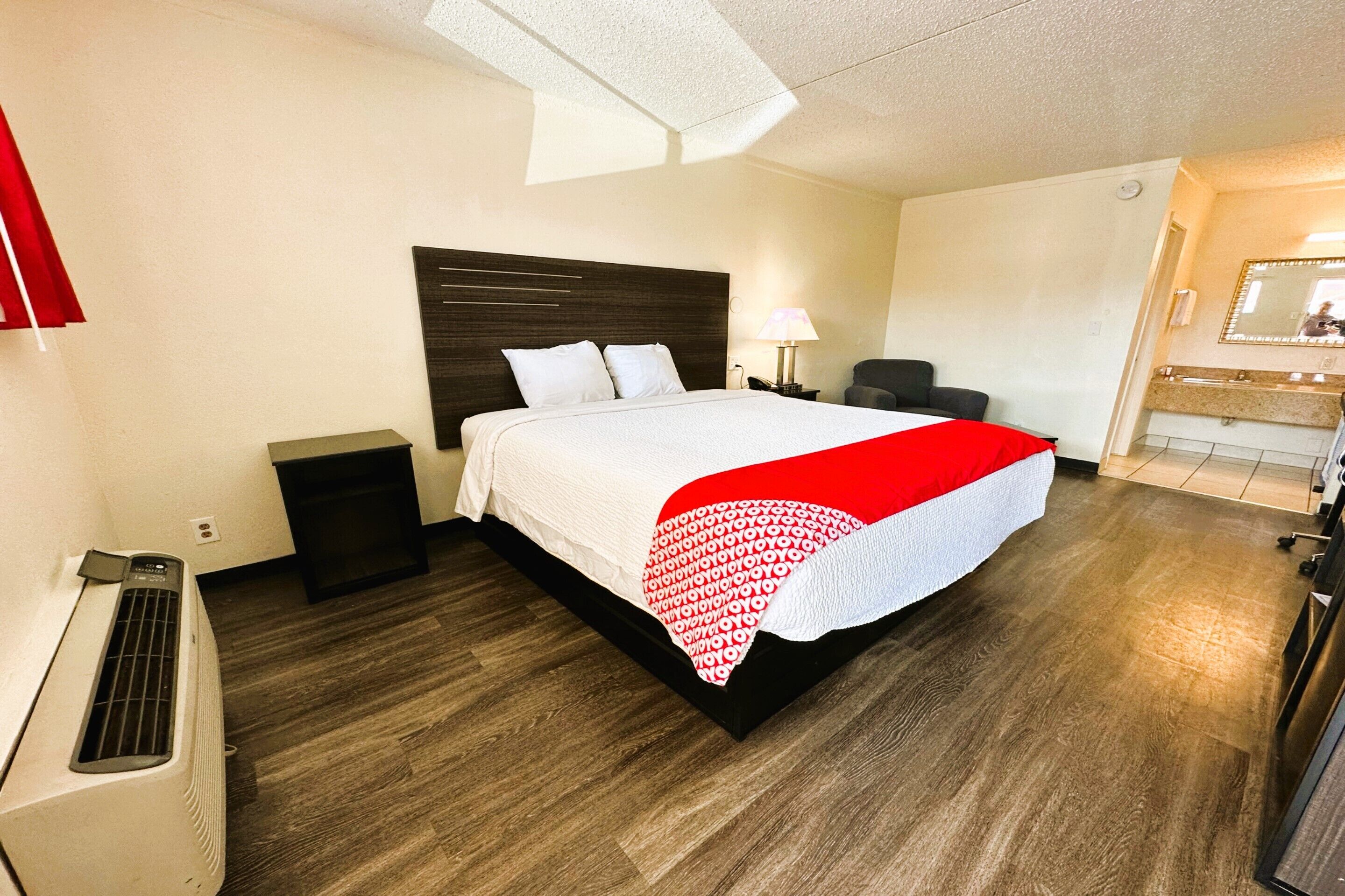 Una habitación de hotel con una cama grande, una mesita de noche, una lámpara, una silla y un espejo.