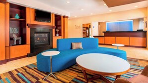 A modern hotel lobby with a blue sofa, a fireplace, a small bar area, and a corner market sign. - Fairfield Inn & Suites Abilene (Abilene)
