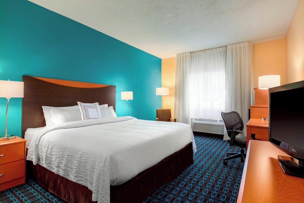 A hotel room with a large bed, a desk with a computer, a chair, and a TV.