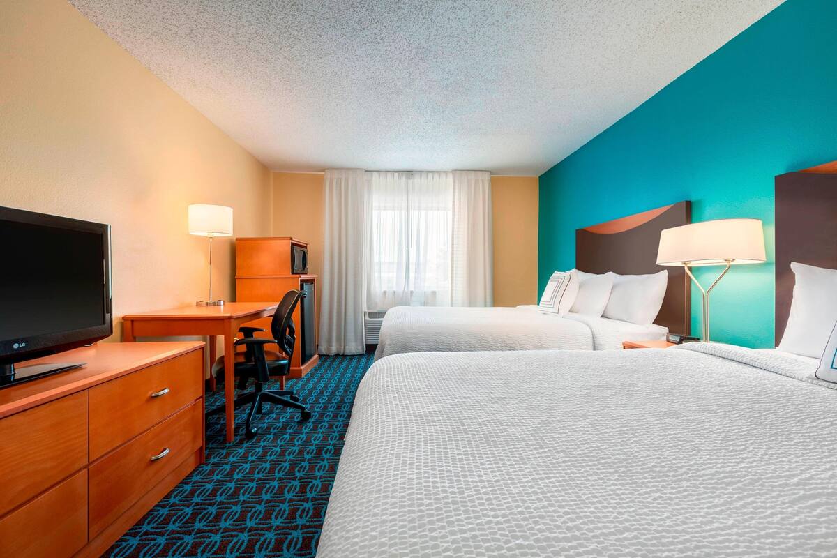 A hotel room with two beds, a desk with a TV, a chair, and a desk lamp.
